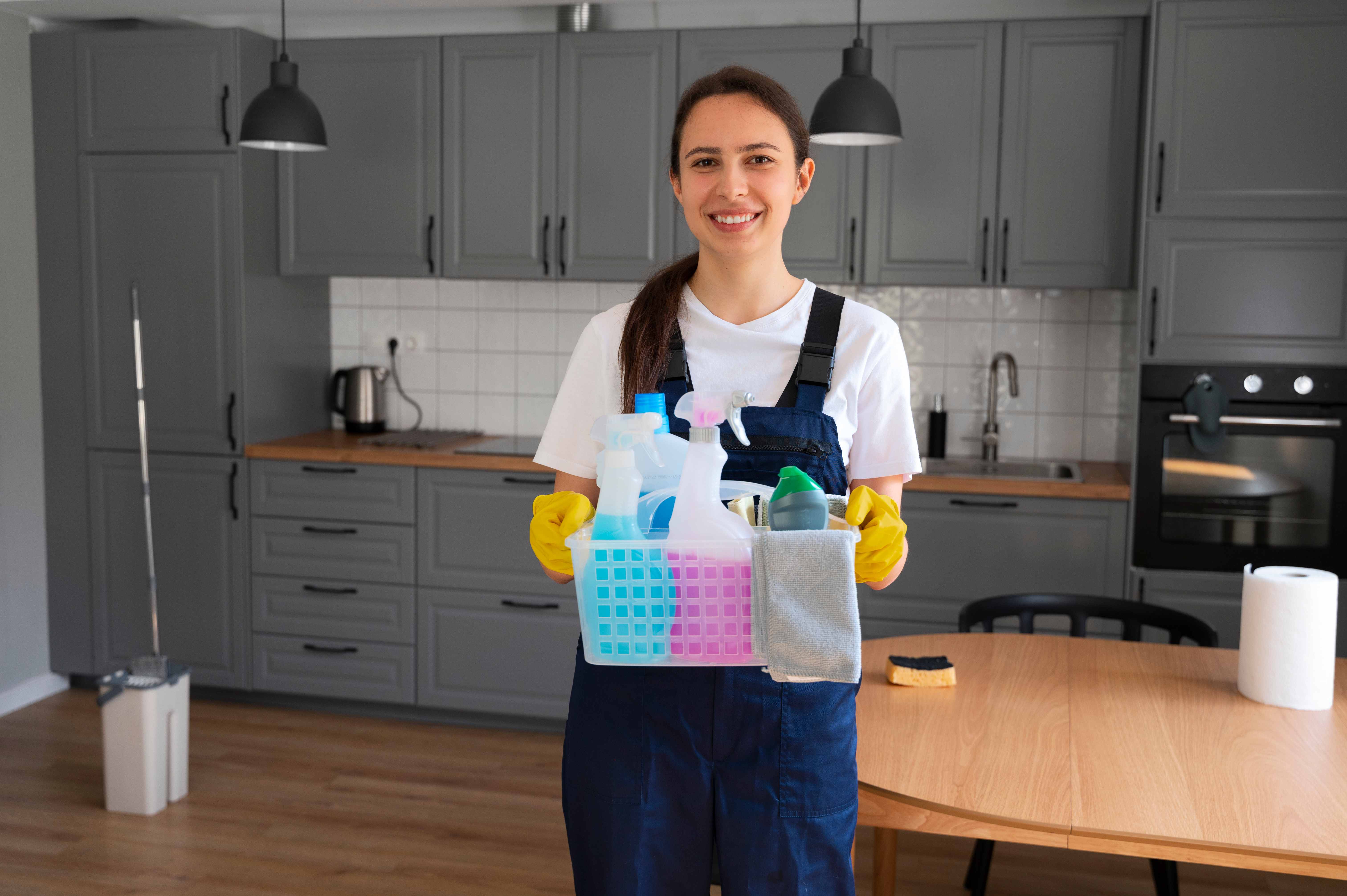 Professional cleaning team member with cleaning supplies in modern kitchen