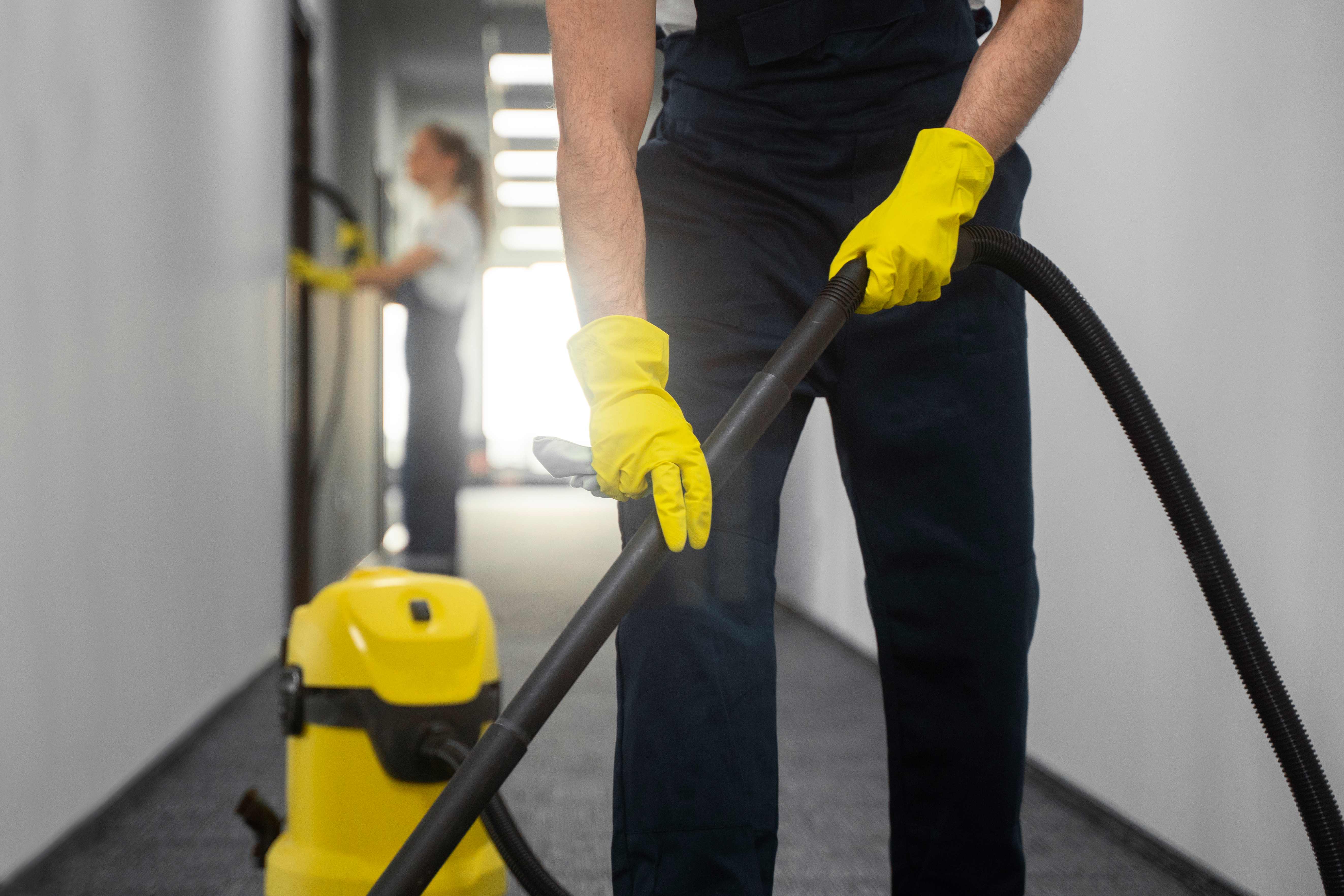 Professional office cleaning services - cleaner using vacuum in modern office hallway